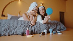Happy female friends lying on a bed applying cosmetic face masks and under-eye patches, laughing and having fun together during a relaxing home spa day and skincare treatment - Powered by Shutterstock - Get 15% off with code: PIKWIZARD15