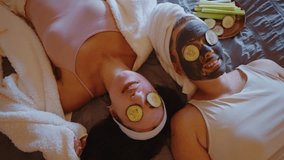 Joyful female friends lying on a bed with facial masks and cucumber slices on their eyes, smiling and relaxing together during a home spa day beauty routine for skincare and wellness - Powered by Shutterstock - Get 15% off with code: PIKWIZARD15