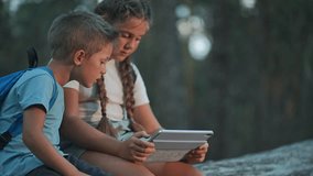 Children using tablet sitting in forest. Boy and girl explore screen content in outdoor nature. Friends interact with technology. Tablet helps children learn. Outdoor moment of learning in forest. - Powered by Shutterstock - Get 15% off with code: PIKWIZARD15