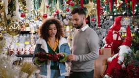 Couple choosing discounted Christmas wreath decoration together in a holiday store - Powered by Shutterstock - Get 15% off with code: PIKWIZARD15