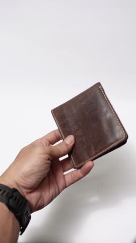 Two hands open an old brown wallet showing it completely empty, representing money shortage, financial struggle, or being broke.