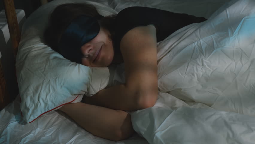 Relaxed woman wearing sleep mask lying in bed at night preparing for deep and healthy sleep