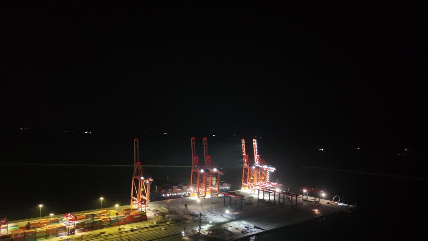 Brightly illuminated cranes unloading a large container ship docked at the commercial port of mersin, turkey, showcasing nighttime industrial activity and global logistic operations
