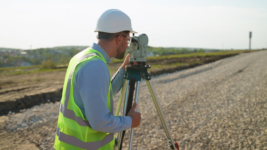 Surveyor engineer using theodolite for topographic measurement on road construction site
