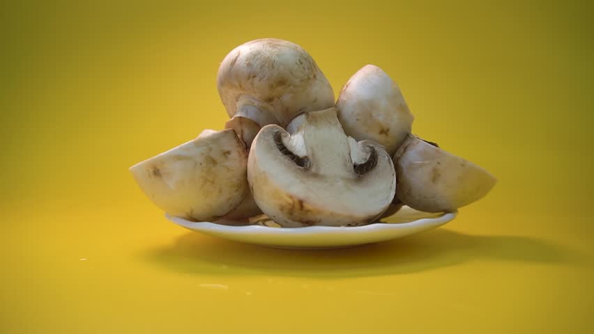 Champignons on a white plate. Halves and slices, studio shooting on a bright yellow background, close-up, me. Hollywood shooting of champignons. Broadway shooting of champignons.