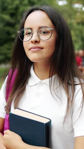 A woman walks through a park with a book in her hands enjoying a sunny day while smiling at the surroundings