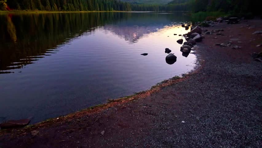 A classic, breathtaking scenic view of the majestic Mount Hood volcano perfectly reflected in the calm, glassy waters of Trillium Lake, illuminated by the warm, golden light of sunrise.