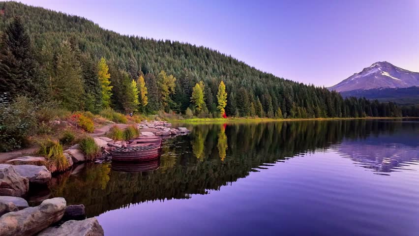 A classic, breathtaking scenic view of the majestic Mount Hood volcano perfectly reflected in the calm, glassy waters of Trillium Lake, illuminated by the warm, golden light of sunrise.