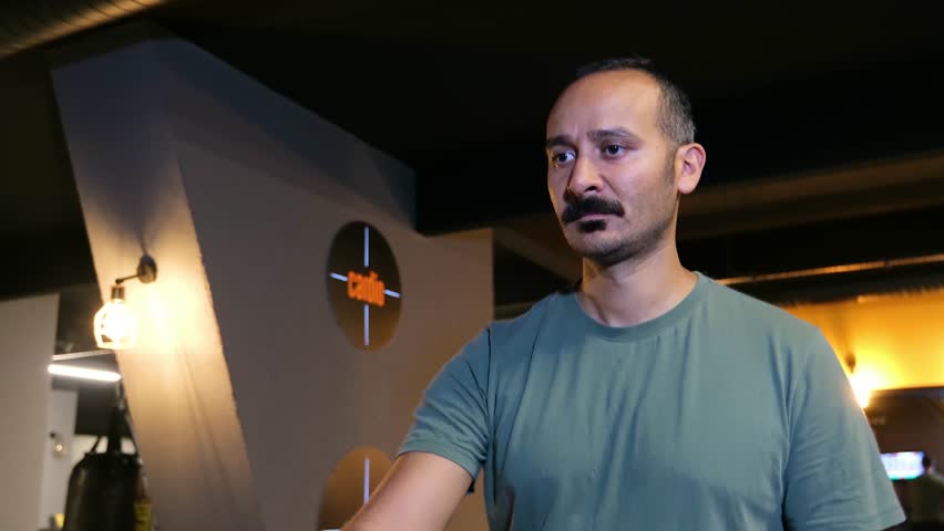 Man in his 30s with a mustache walking on a treadmill in slow motion. 4K front view (Shot 2) of a tanned man doing a warm-up or cool-down walk in a fitness center.