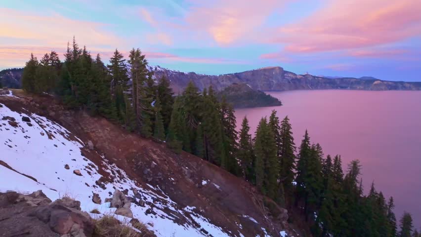 A stunning aerial perspective showcasing the deep blue Crater Lake and its iconic Wizard Island, bathed in the vibrant, colorful hues of a dramatic sunset