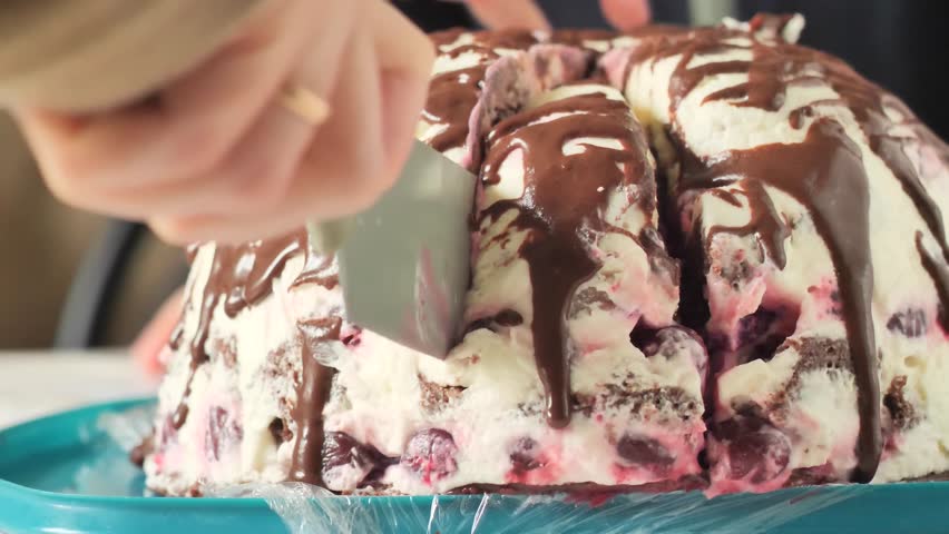 Slicing chocolate volcano berry cake - homemade Pancho cake, showing the white sour cream frosting, berries, and chocolate drizzle