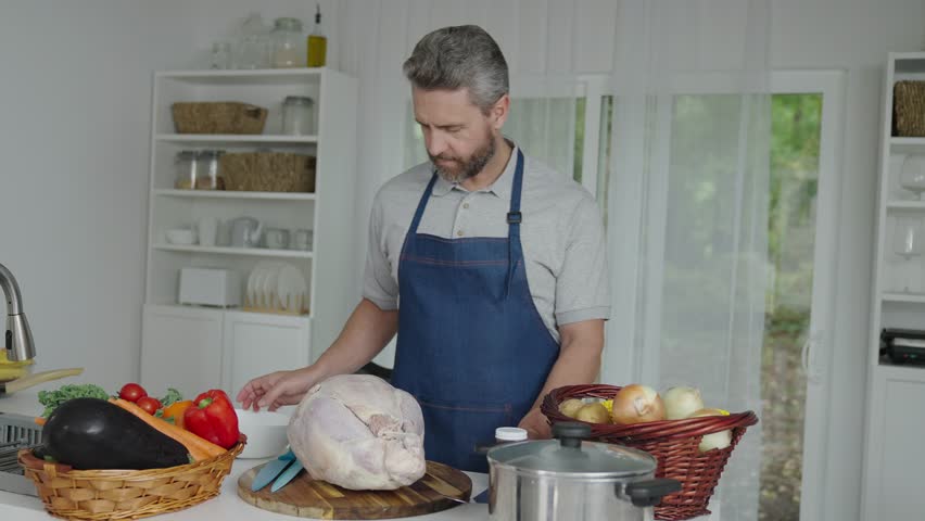 Thanksgiving day dinner. Hispanic man cooking in kitchen. Thanksgiving dinner food. Man cooking food. Cooking turkey for Thanksgiving. Mature man in apron with turkey. Home menu. Slow motion