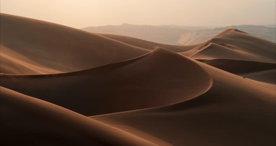 Majestic desert dunes undulate under a soft twilight sky Wind gently blows sand over the smooth, curving ridges, creating a tranquil scene