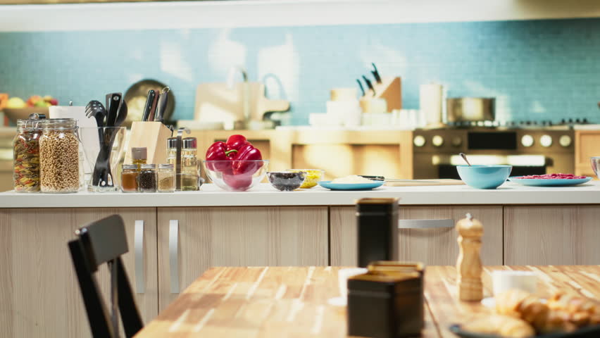 Empty cozy kitchen with a pizza prep area ready for cooking on the isle. Fresh ingredients like mozzarella and tomato sauce rest on the counter beside containers and utensils for homemade meal.