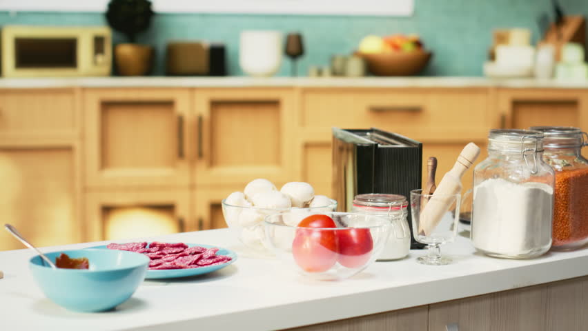 Comfortable kitchen setup with pizza ingredients on a modern countertop. Bowls of cheese, tomatoes and pepperoni sit beside spices and kitchenware, ready for a fun weekend activity of cooking.