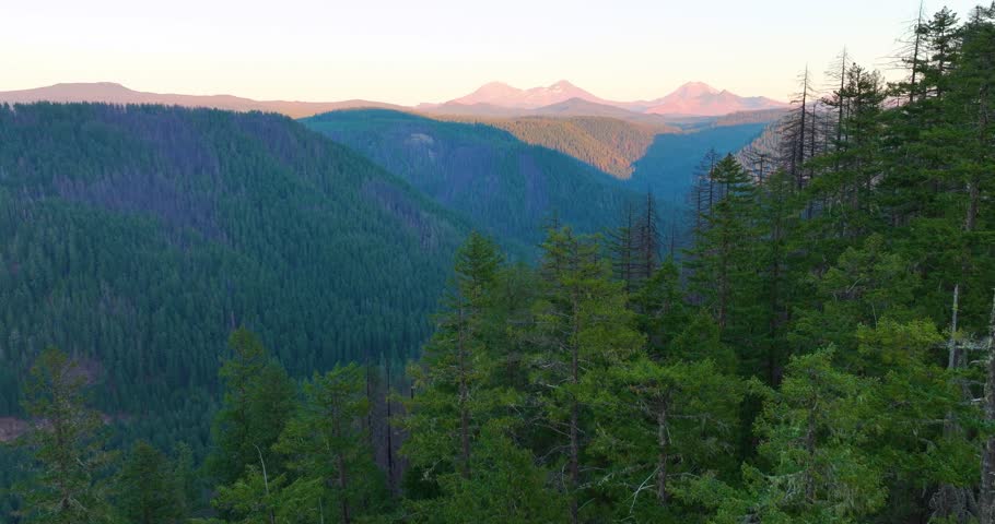 Drone shot of Three Sisters volcanic peaks glowing above dense forest at sunset