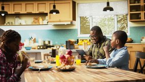 African american dad on tablet multitasking and chatting with his son, serving breakfast with his family and eating good homemade food in the kitchen. Togetherness and joy. Camera A. - Powered by Shutterstock - Get 15% off with code: PIKWIZARD15