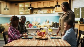 African american woman pouring orange juice in glasses at the breakfast table, serving a rich homemade meal with fruits and pastry next to eggs. Cute morning routine for the family. Camera A. - Powered by Shutterstock - Get 15% off with code: PIKWIZARD15