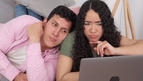Happy young couple lying on the sofa at home while using a laptop computer. They are watching videos, browsing social media and smiling - Powered by Shutterstock - Get 15% off with code: PIKWIZARD15