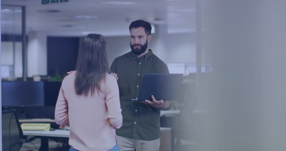 Man gesturing with laptop in business, starting data overlays drifting across faces showing metrics. Collaboration, duo, office, workspace, corporate, communication, dialogue