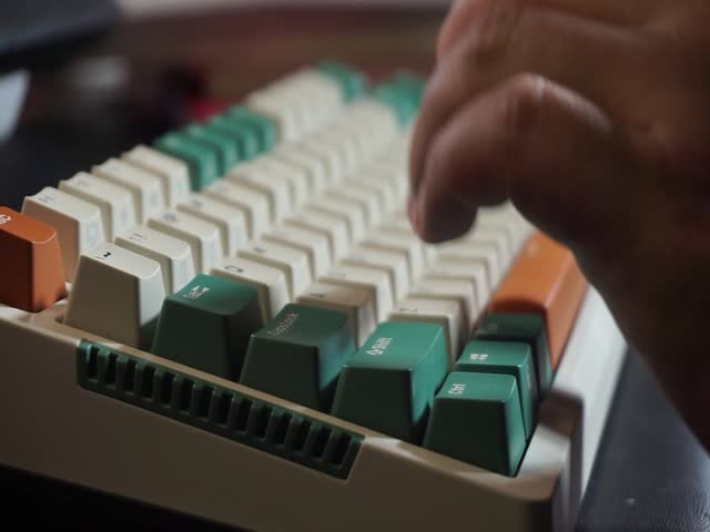 Typing on colorful keyboard with green, white, and orange keycaps, closeup fingers pressing keys under ambient light, creative tech aesthetic.