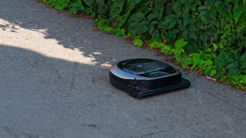 A robotic vacuum cleaner drives down the street, cleaning dirt from roads. A robotic uprising or a way to help with everyday tasks.