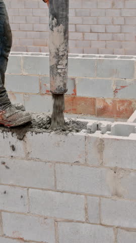 Construction worker skillfully fills concrete into blocks while building structure on works day outdoors.