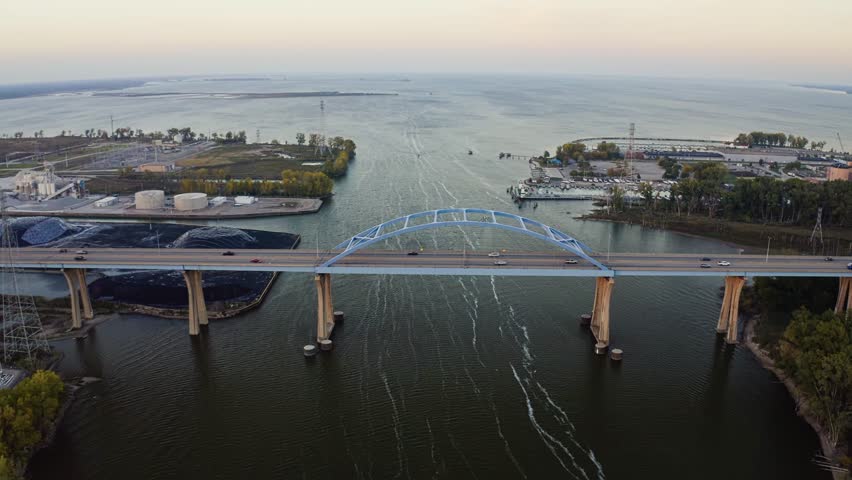 The Leo Frigo Memorial Bridge arches across the Fox River toward the vast waters of Green Bay, its pale blue steel contrasting with calm evening reflections and the city’s industrial waterfront.