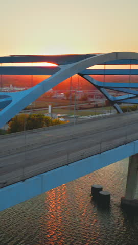 The sun dips low behind the sweeping blue arches of the Leo Frigo Memorial Bridge in Green Bay, Wisconsin, casting warm reflections across the Fox River and moving evening traffic.