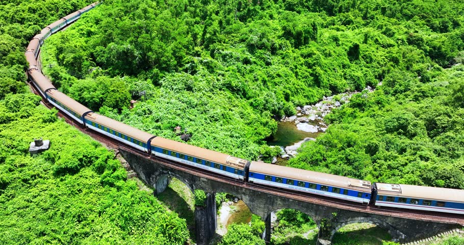 Flying above train rushing along the picturesque Hai Van Pass, Hue, Vietnam. Spectacular view of train crossing the dense tropical forest covering the remote Asian island. Beautiful shoreline.