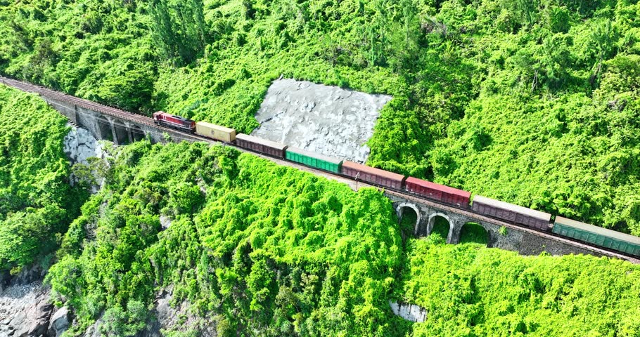 Flying above train rushing along the picturesque Hai Van Pass, Hue, Vietnam. Spectacular view of train crossing the dense tropical forest covering the remote Asian island. Beautiful shoreline.
