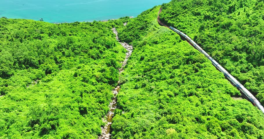 Flying above train rushing along the picturesque Hai Van Pass, Hue, Vietnam. Spectacular view of train crossing the dense tropical forest covering the remote Asian island. Beautiful shoreline.
