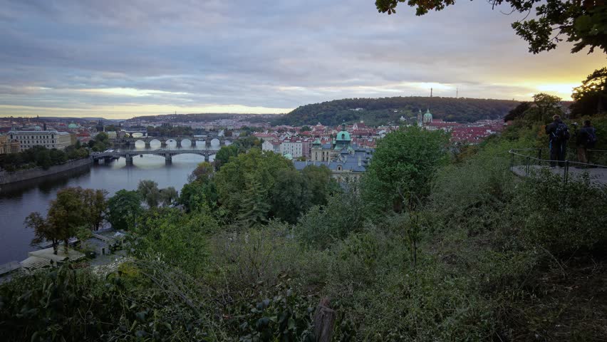 Scenery of Vltava River under golden sunset sky, with sightseeing boats crusing under the bridges and tourists walking on the famous landmark Charles Bridge, in Prague, Cezch Republic, Europe