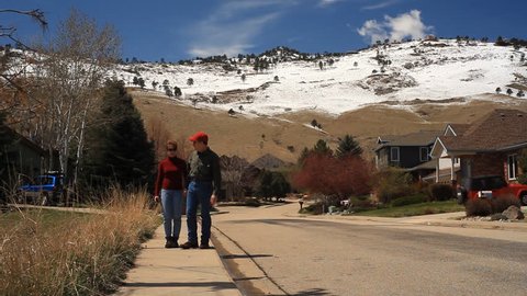 A man and a woman strolling down the sidewalk of a neighborhood in the foothills of Boulder Colorado.