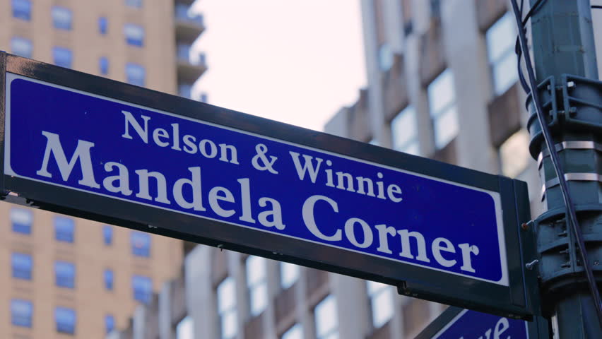 Close up of the Nelson and Winnie Mandela Corner street sign in Manhattan New York, with modern buildings in the background representing urban culture and city heritage.