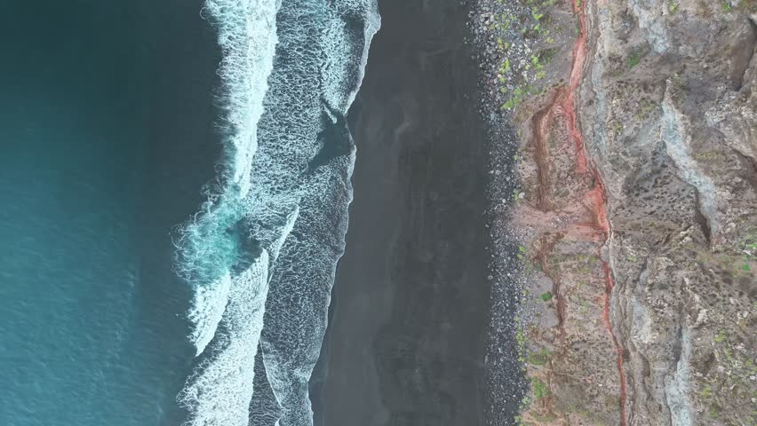 Top-down drone view of beautiful steep coastal cliffs with reddish geological rock layers with Atlantic Ocean waves, Tenerife, Canary Islands, Spain.