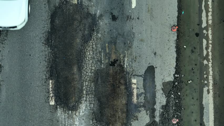 Cracks and erosion on the asphalt road, as seen from above, reveal poor maintenance, urban planning issues, road safety concerns, fiscal shortfalls, environmental impact, and demand for upgrades.
