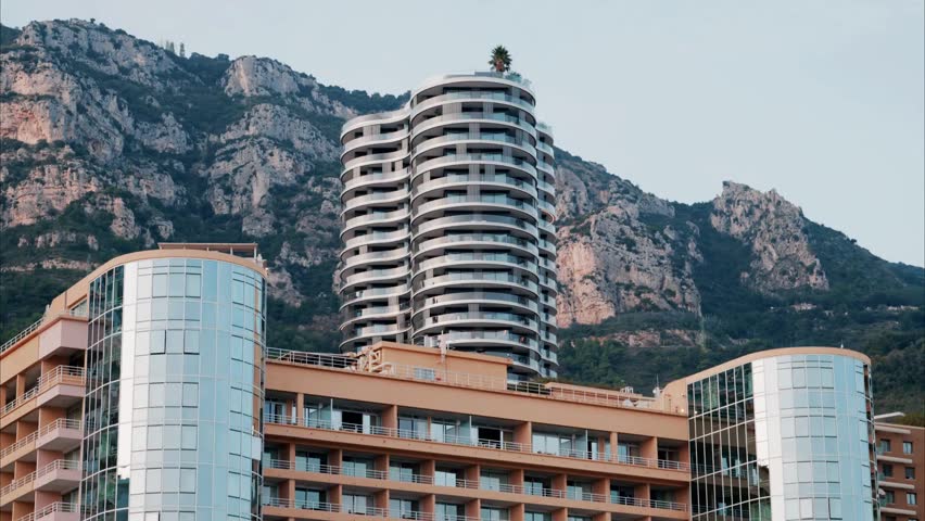 Aerial view of Monaco’s skyline in daylight, showcasing luxurious buildings, the harbor, and the deep blue Mediterranean Sea along the glamorous French Riviera.