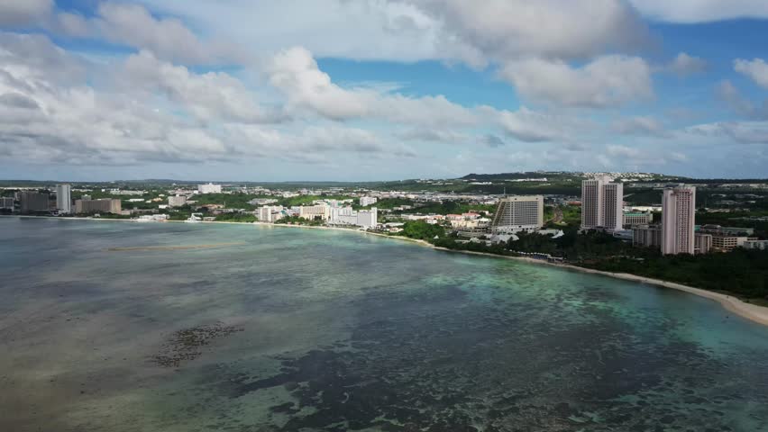 Panoramic aerial hyper lapse of stunning Tumon Bay reef with coastal hotel resorts and moving clouds during daytime - Guam, USA