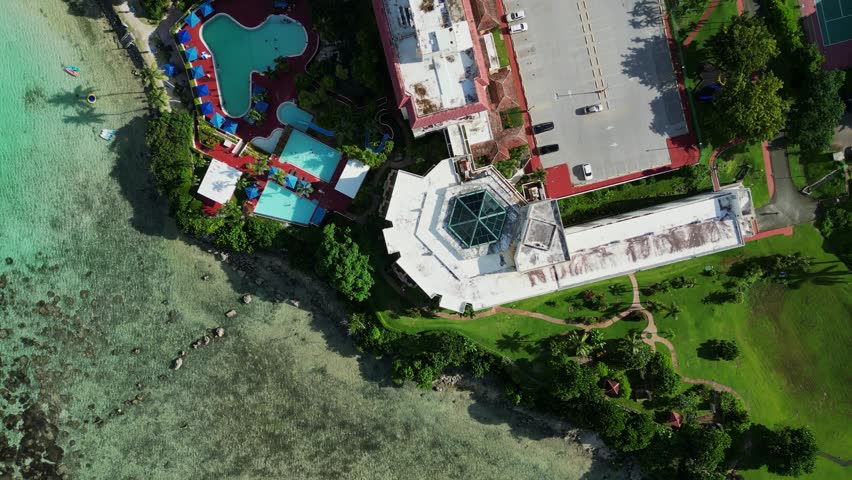 Aerial top-down flyover of tropical island resort with lush greenery, a swimming pool, and hotel building at Guam, USA.