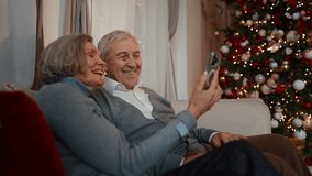 Grandparents calling by video in smartphone in Christmas vacation, happy people. Portrait of elderly spouses celebrating winter holidays at home and congratulating family online, distant communication - Powered by Shutterstock - Get 15% off with code: PIKWIZARD15