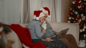 Christmas and New year, elderly spouses in cozy interior, video call by laptop. Beautiful Xmas decoration in living room, distant communication with family and friends, funny Santa hats and smiles - Powered by Shutterstock - Get 15% off with code: PIKWIZARD15