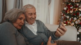 Merry Christmas time, portrait of grandparents calling by video in smartphone. Elderly people celebrating winter holidays at home together, pretty aged man and woman in beautiful decorated room - Powered by Shutterstock - Get 15% off with code: PIKWIZARD15