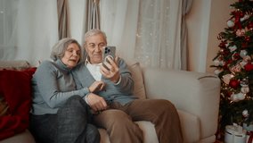 70-years-old spouses chatting online by video call in smartphone from home. Grandparents celebrating fabulous winter holidays, Christmas and new year vacation, cozy home interior with Christmas tree - Powered by Shutterstock - Get 15% off with code: PIKWIZARD15