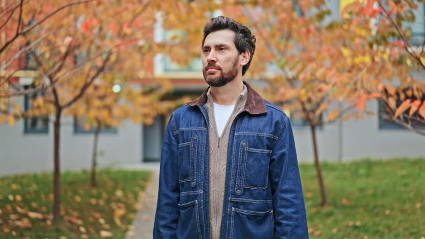 Mature man stands among autumn trees, expressing confidence, happiness. Smiles brightly at camera, conveying positive emotions outdoors. Joy and contentment fill scene with a charming, relaxed vibe.