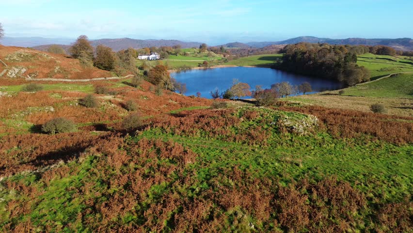 Cinematic drone swooping over autumn hills towards a peaceful Lake District manor and blue lake
