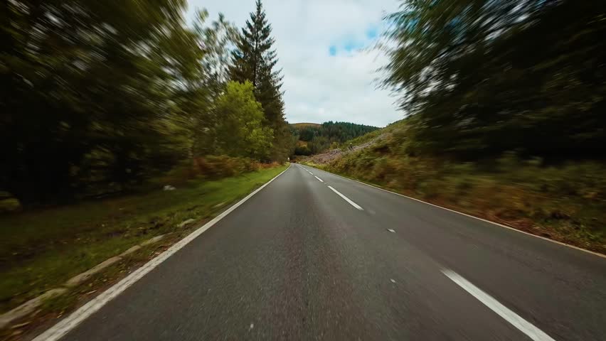 Voyager driving along countryside road stretching between forested hills and green meadows POV. Pathfinder cruising down quiet rural highway lined with trees and brush first person view. Adventurer