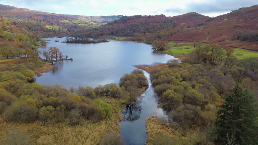 Cinematic drone swooping over a peaceful lake surrounded by autumn hills in the Lake District