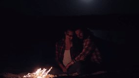A couple sits close together, cuddling by a campfire under the moonlit night sky, captured in slow motion. Perfect for romantic, camping, or outdoor-themed content that emphasizes warmth and intimacy. - Powered by Shutterstock - Get 15% off with code: PIKWIZARD15