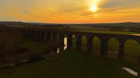 Long railway viaduct extending over green valley under golden sky. Historic stone viaduct glowing under fading sun. Endless brick bridge arching across vast countryside in warm twilight hues - Powered by Shutterstock - Get 15% off with code: PIKWIZARD15